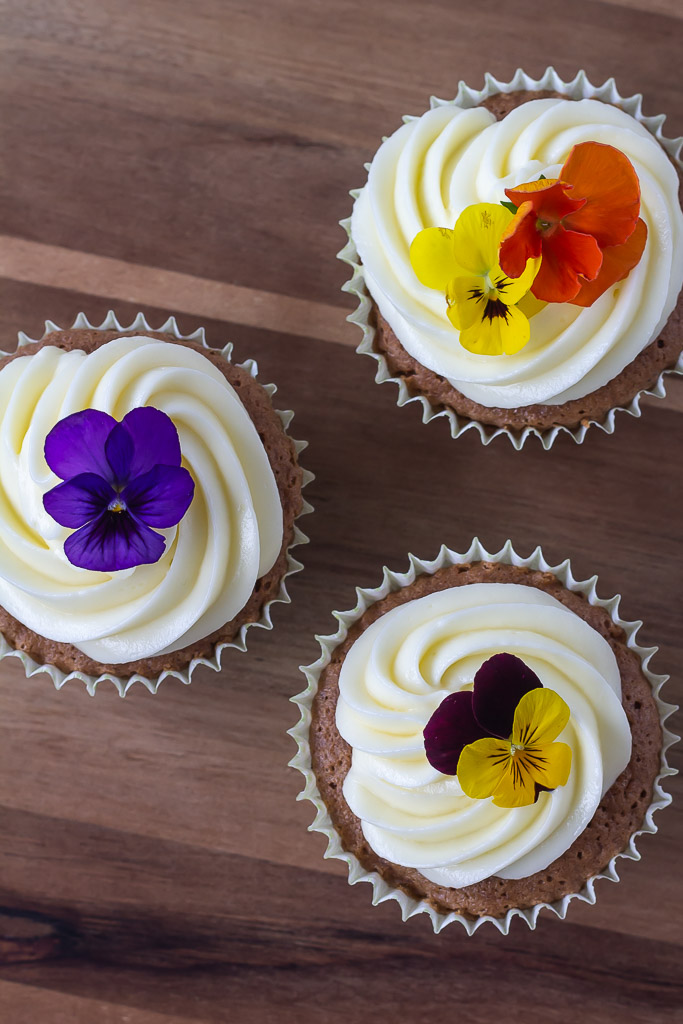 Gulerodsmuffins med ostecreme og pyntet med blomster set oppefra